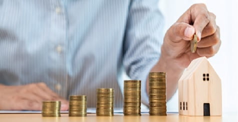 kleines Modellholzhäuschen, neben dem jemand Münzen stapelt